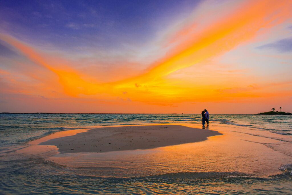 Couple shares a romantic moment on a serene tropical beach at sunset, surrounded by vibrant colors.